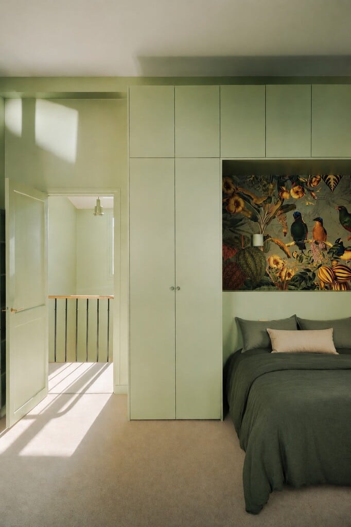 Light green bedroom painted in Farrow & Ball Cooking Apple Green with built-in wardrobes and a botanical wallpaper panel
