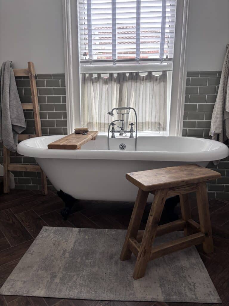 The Dancing Woodman James bath caddy across a white roll-top bath with a rustic wooden stool and ladder