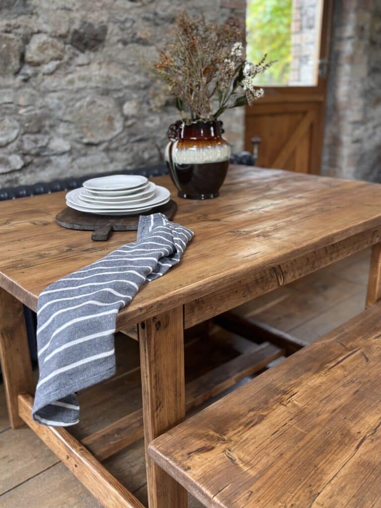 The Dancing Woodman rustic pine dining table and bench against a stone wall