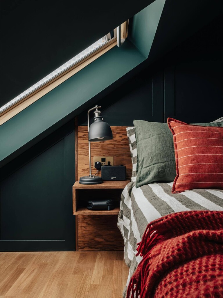 Dark green loft bedroom painted in Farrow & Ball Studio Green and Monkey Puzzle with a rust striped cushion and oak bedside shelf