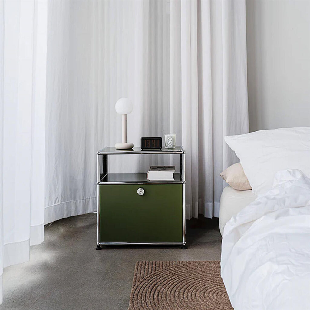 Green and white bedroom with an olive green USM Haller side table, white curtains, white bedding and a globe table lamp