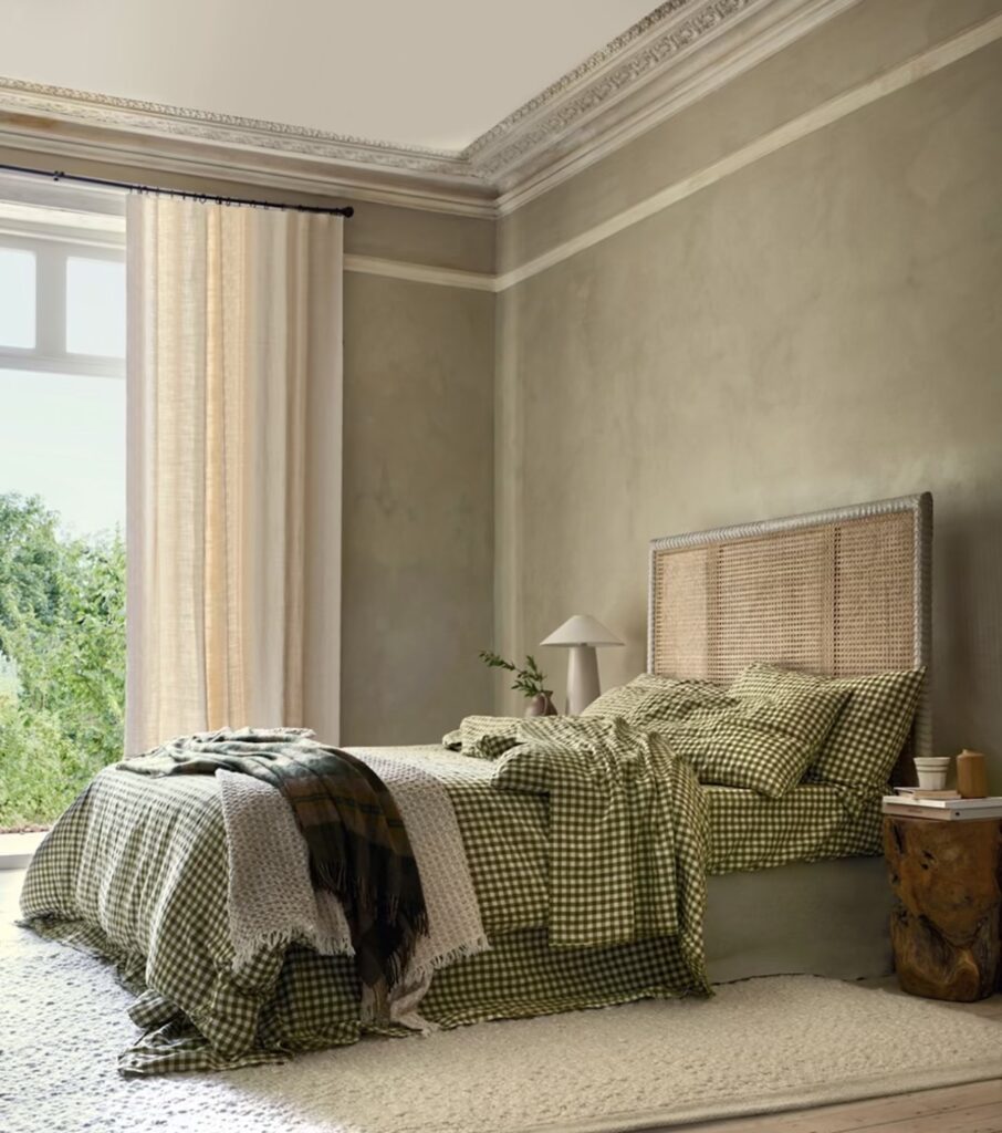 Olive green bedroom with olive gingham linen bedding, a cane headboard, tartan throw and earthy plaster-effect walls