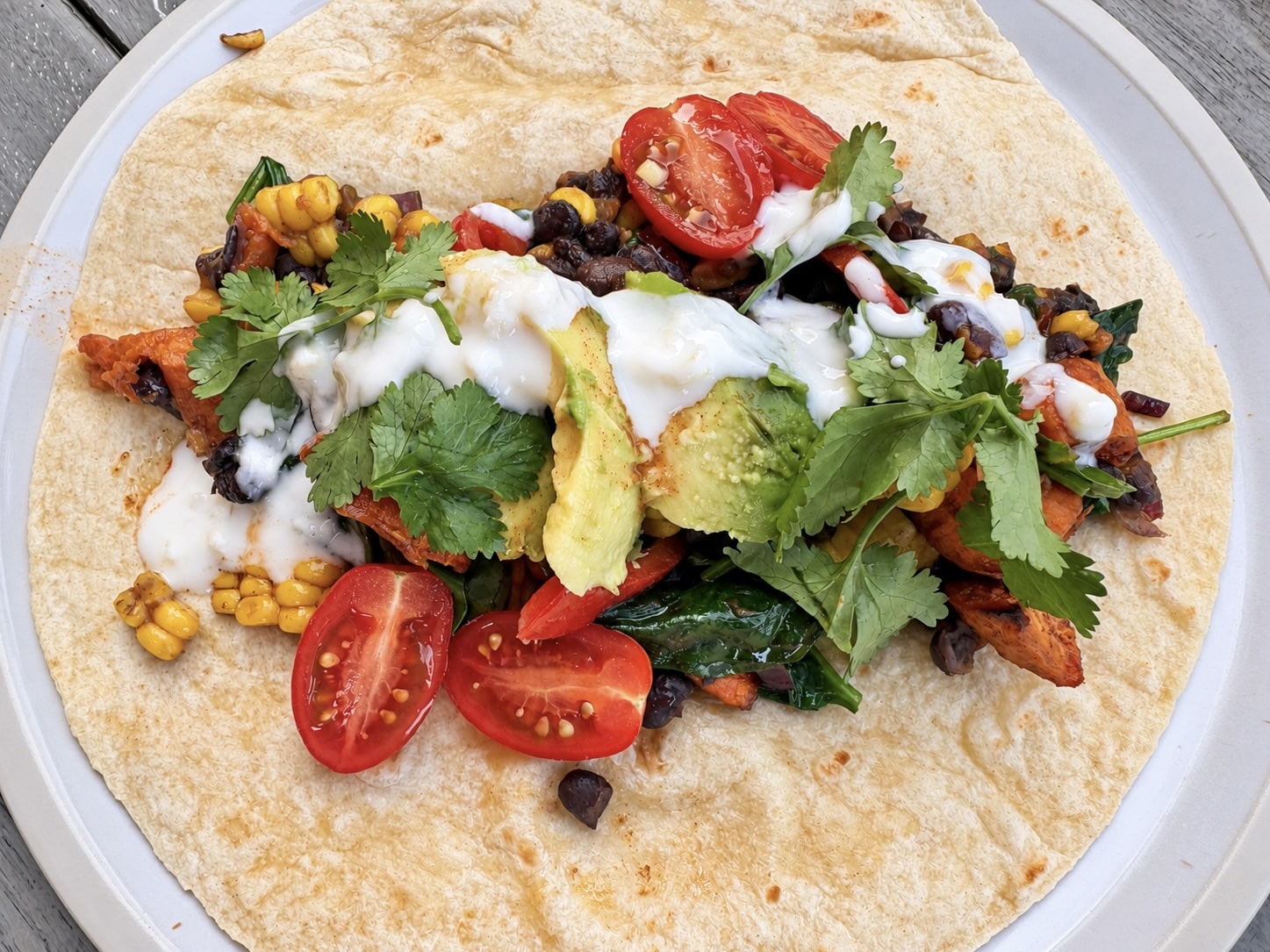 Vegan breakfast burritos with roasted sweet potato and black beans, cut in half on a rustic wooden board with salsa and a dairy-free herb dip
